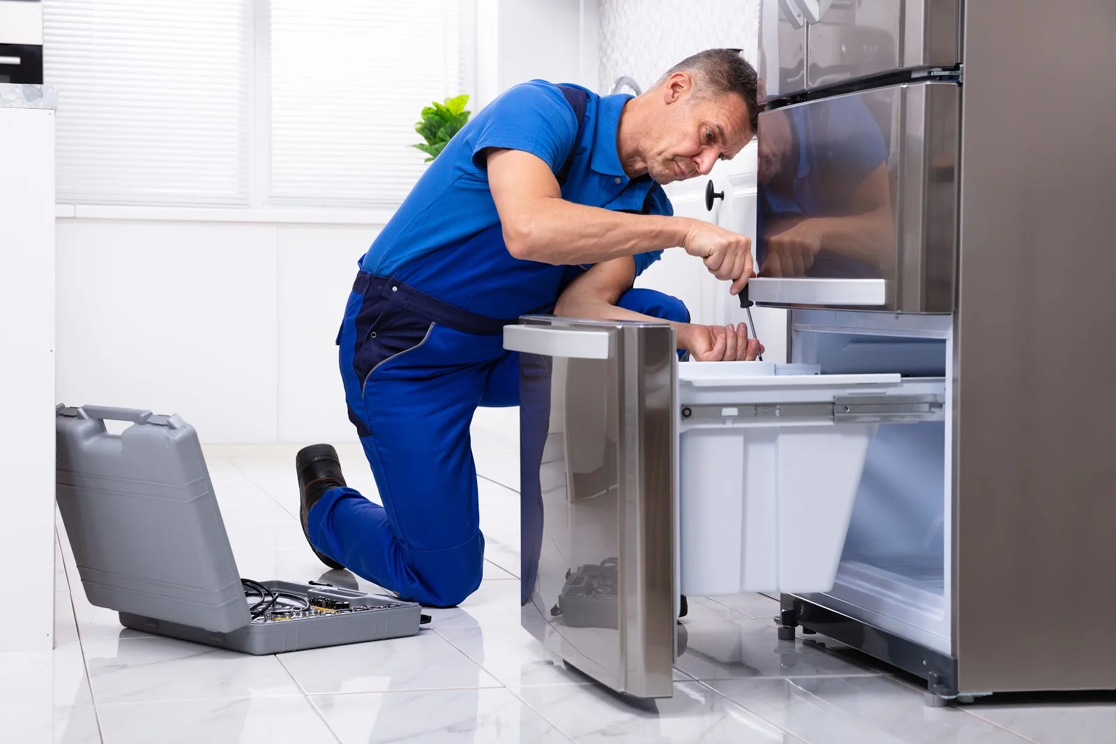 Appliance technician repairing a refrigerator in a residential kitchen